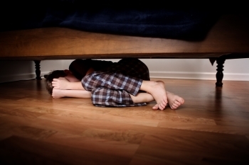 Bilde av person som gjemmer seg under et møbel.